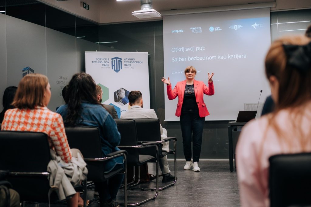 A women standing in front of a white board with her hands up - lecturing female students for starting a career in cybersecurity in Serbia