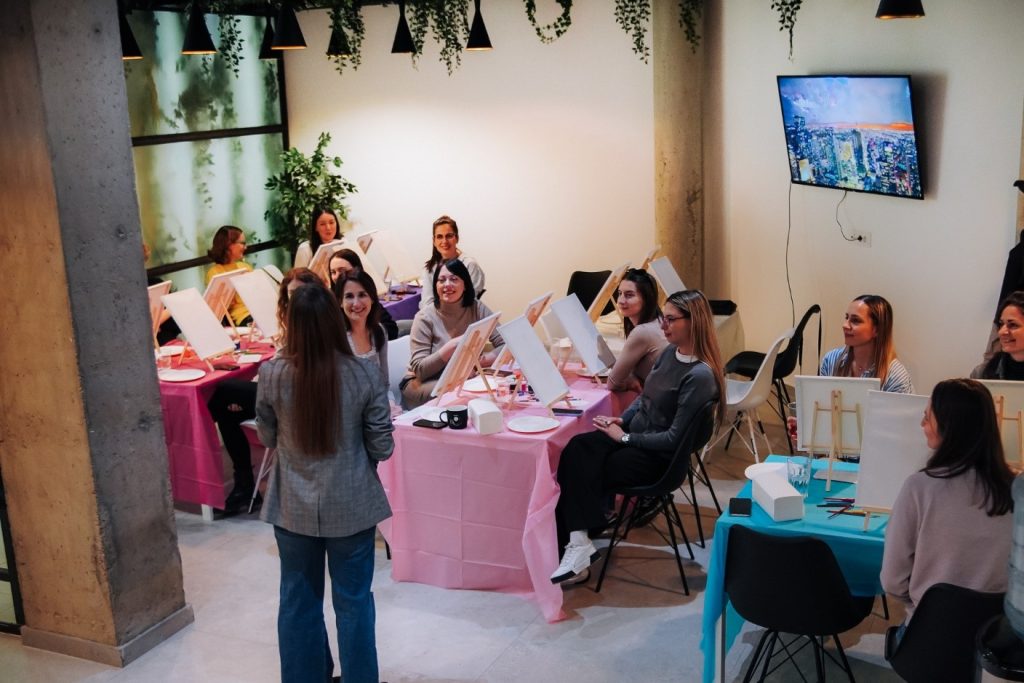 A group of women sitting at tables at a Paint And Wine company event.